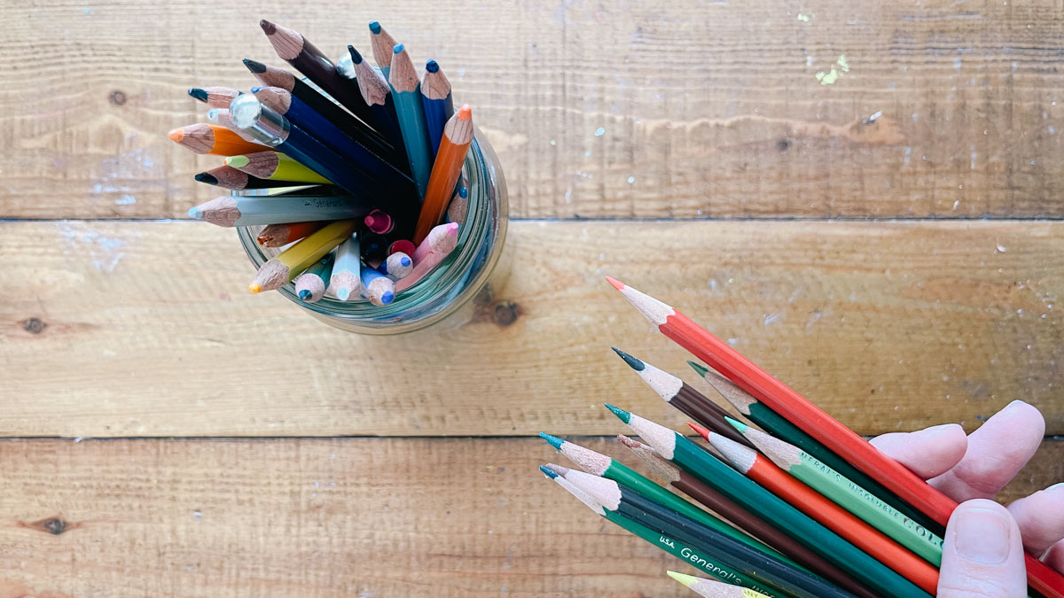 A hand holding colored pencils.